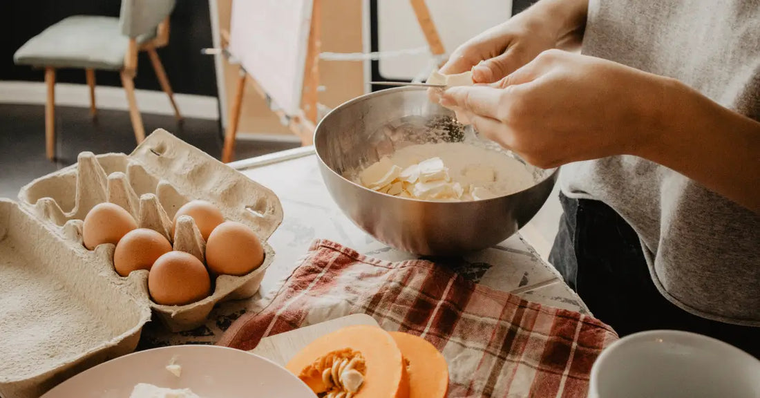 Person baking with protein powder in a mixing bowl, surrounded by eggs and other baking ingredients.