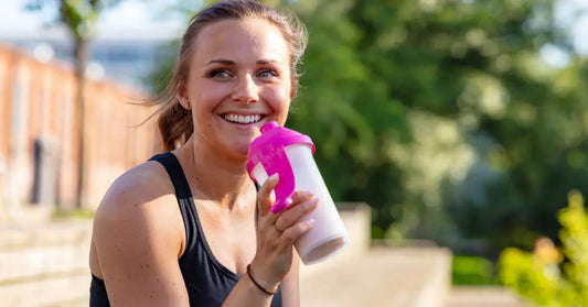 Image of a woman smiling while holding a shaker bottle, considering if you should take protein powder on rest days.