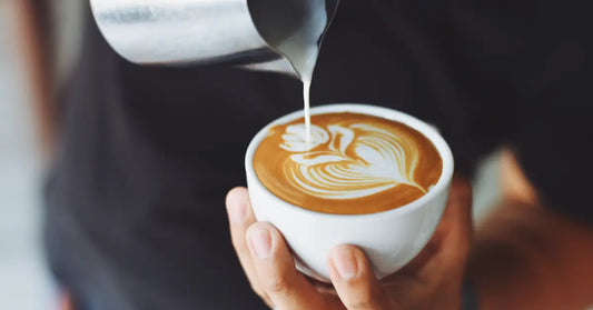 Close-up of a barista skillfully creating latte art by pouring steamed milk into a cup of espresso. Keywords can you put protein powder in coffee.