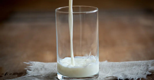 Milk pouring into a clear glass on a rustic wooden table, demonstrating a preferred liquid for mixing with protein powder