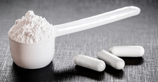 Scoop of white creatine powder next to white capsules, demonstrating the combination of creatine with protein powder.