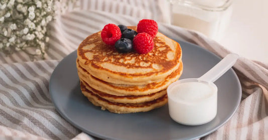 Stack of pancakes topped with berries next to a scoop of protein powder, illustrating the addition of protein powder to pancake mix.