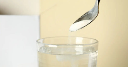 spoon is pouring white protein powder into a glass of clear liquid